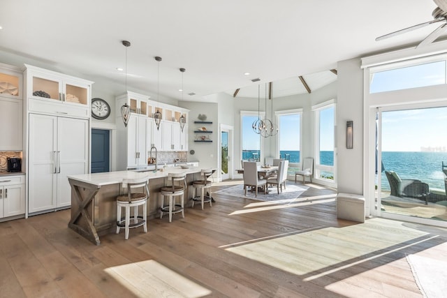 kitchen with a water view, a kitchen island with sink, white cabinets, and decorative light fixtures