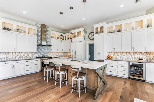 kitchen with decorative light fixtures, white cabinets, wine cooler, premium appliances, and wall chimney range hood