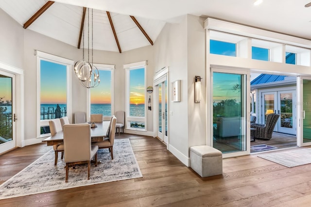 dining space with french doors, a water view, a chandelier, high vaulted ceiling, and hardwood / wood-style floors