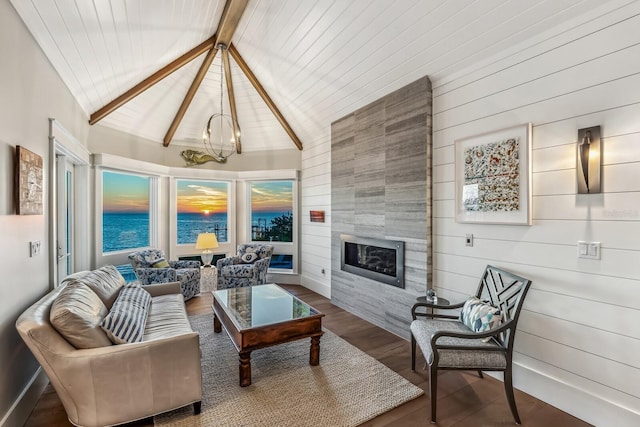 living room featuring vaulted ceiling with beams, a water view, a notable chandelier, a tiled fireplace, and hardwood / wood-style floors