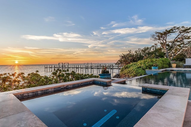 pool at dusk featuring a water view and a jacuzzi