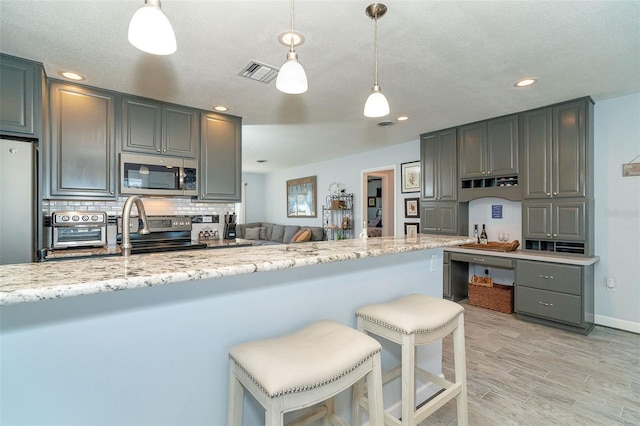 kitchen with stainless steel appliances, light stone counters, tasteful backsplash, and hanging light fixtures