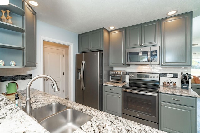 kitchen featuring stainless steel appliances, sink, backsplash, and light stone counters