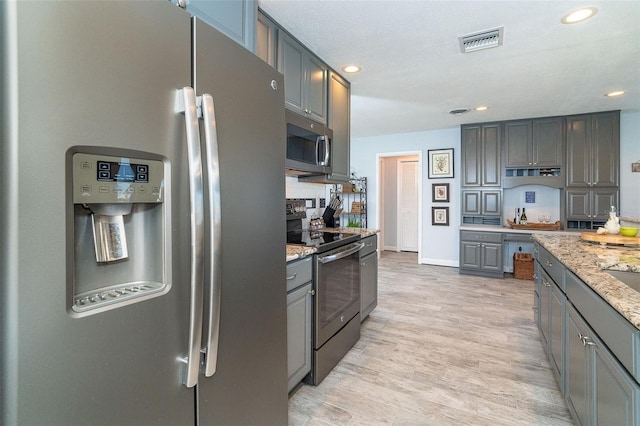 kitchen featuring gray cabinetry, stainless steel appliances, light hardwood / wood-style flooring, and light stone countertops