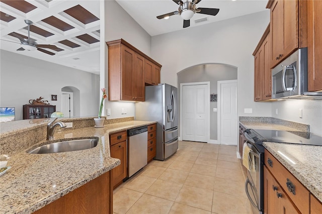 kitchen with coffered ceiling, appliances with stainless steel finishes, sink, light stone counters, and beamed ceiling