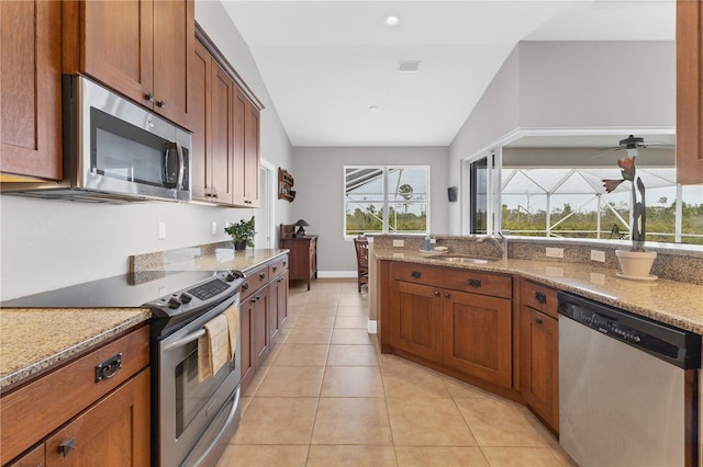 kitchen with lofted ceiling, sink, appliances with stainless steel finishes, light tile patterned floors, and light stone counters