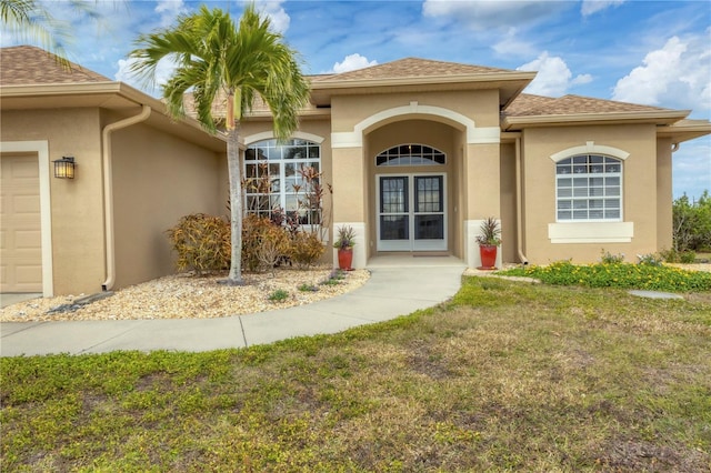 116 Hercules Dr, Rotonda West, FL 33947 - doorway to property featuring stucco siding, a lawn, an attached garage, and roof with shingles
