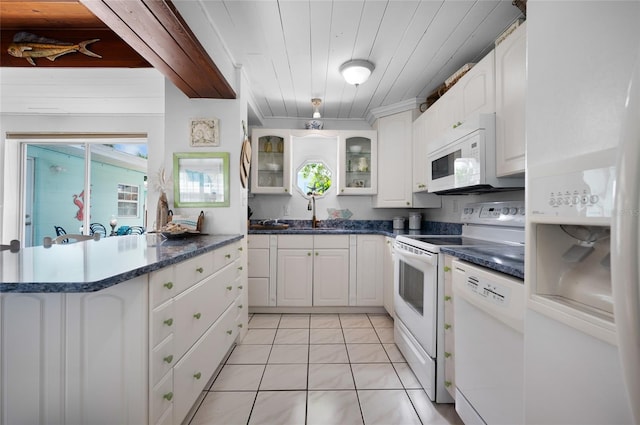 kitchen with a peninsula, white appliances, a sink, white cabinetry, and glass insert cabinets