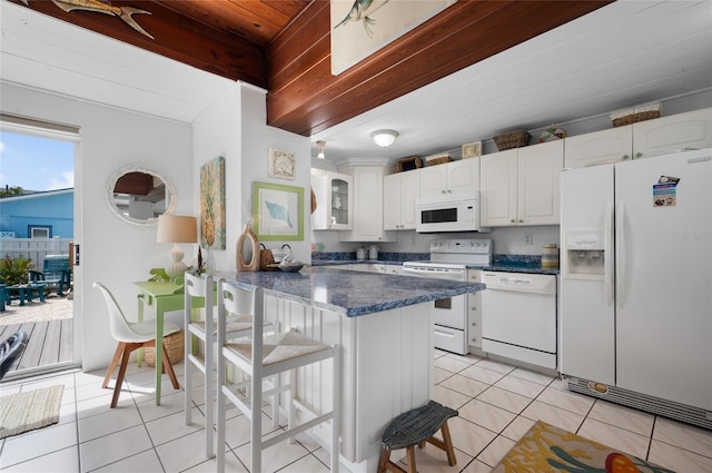 kitchen with a breakfast bar area, light tile patterned floors, white cabinetry, white appliances, and beamed ceiling