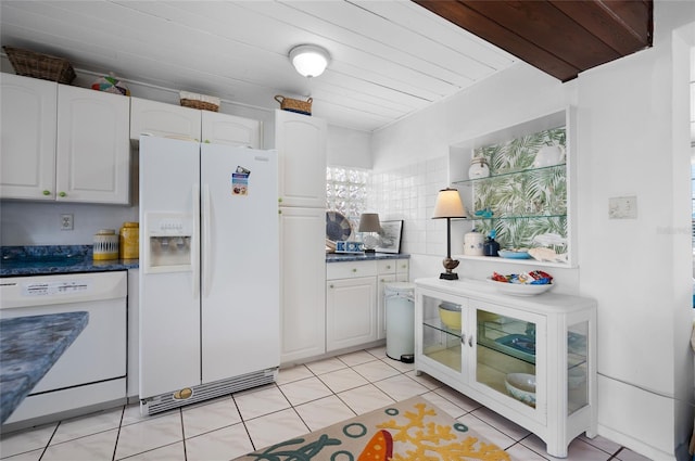 kitchen featuring dark countertops, white appliances, light tile patterned floors, and white cabinetry