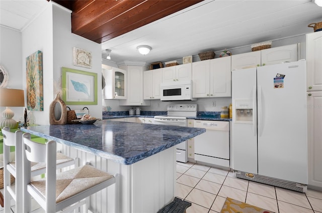 kitchen featuring light tile patterned floors, a peninsula, white appliances, white cabinetry, and dark countertops