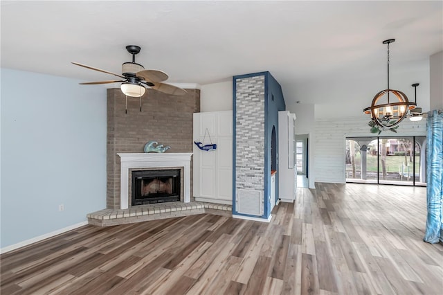 unfurnished living room with a brick fireplace, ceiling fan with notable chandelier, and light hardwood / wood-style flooring