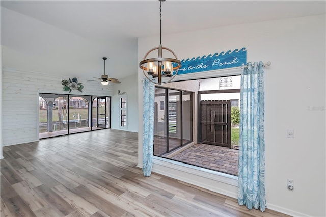 spare room featuring ceiling fan with notable chandelier, wood-type flooring, and wooden walls