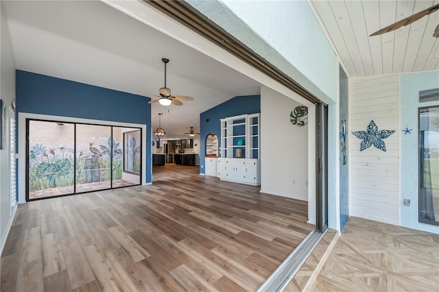 unfurnished living room with vaulted ceiling, ceiling fan, light hardwood / wood-style floors, and wood walls