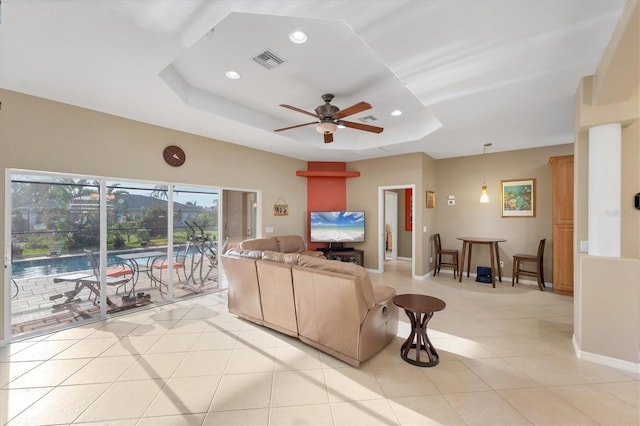 living room featuring light tile patterned flooring, ceiling fan, and a tray ceiling