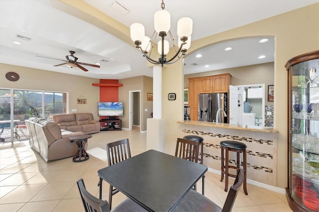 tiled dining space with ceiling fan with notable chandelier and a raised ceiling