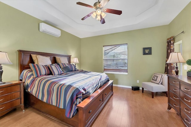 bedroom with light wood-type flooring, a wall mounted AC, a raised ceiling, and ceiling fan