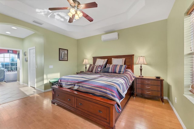 bedroom featuring light wood-type flooring, an AC wall unit, ceiling fan, and a tray ceiling