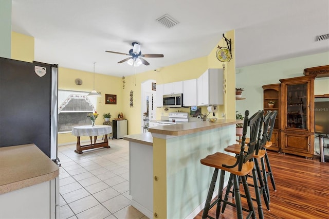 kitchen featuring a breakfast bar area, hanging light fixtures, appliances with stainless steel finishes, kitchen peninsula, and white cabinets