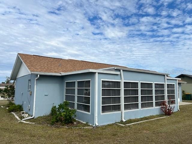 view of side of home featuring a shingled roof, a lawn, and stucco siding