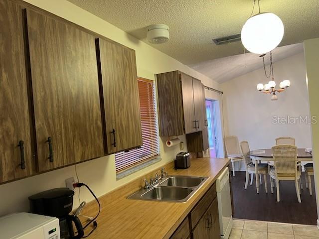 kitchen featuring light tile patterned flooring, white appliances, a sink, light countertops, and decorative light fixtures