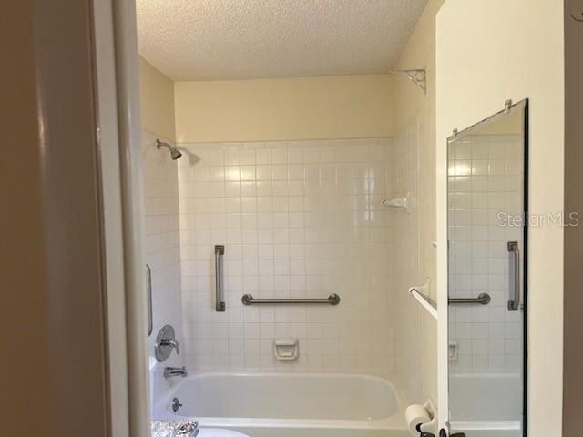 bathroom with washtub / shower combination and a textured ceiling