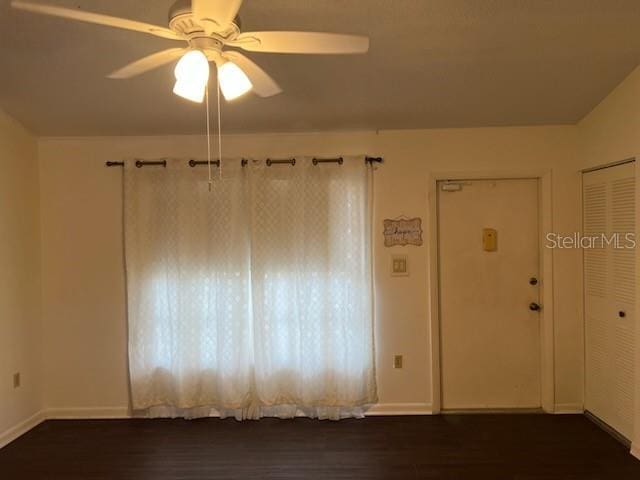 unfurnished room with a ceiling fan, dark wood finished floors, and baseboards