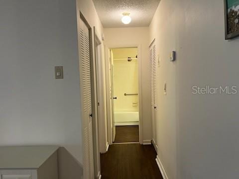 hall with baseboards, dark wood-type flooring, and a textured ceiling