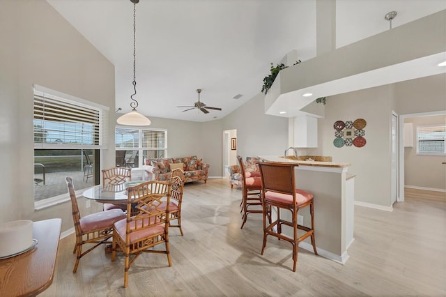 dining area with ceiling fan, sink, light hardwood / wood-style flooring, and high vaulted ceiling