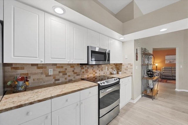 kitchen with lofted ceiling, tasteful backsplash, light stone countertops, stainless steel appliances, and white cabinets