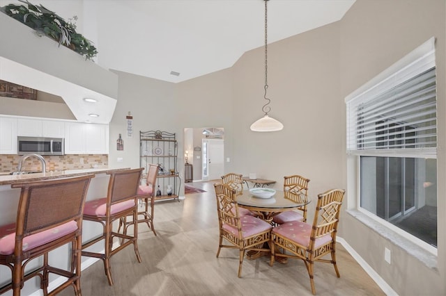 dining room featuring high vaulted ceiling, sink, and light hardwood / wood-style flooring