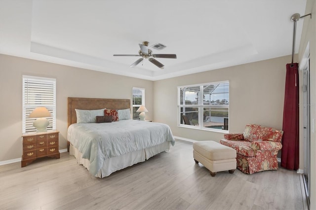 bedroom featuring ceiling fan, light hardwood / wood-style floors, and a tray ceiling