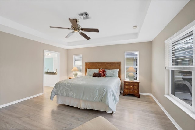 bedroom featuring a raised ceiling, ceiling fan, connected bathroom, and light hardwood / wood-style flooring