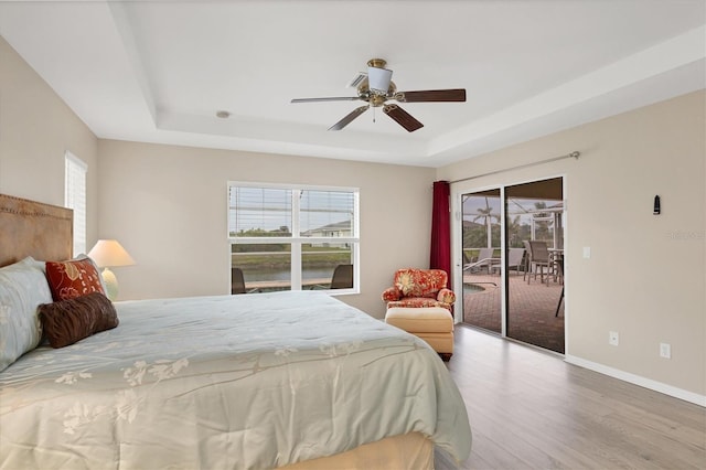 bedroom featuring a raised ceiling, access to exterior, multiple windows, and ceiling fan