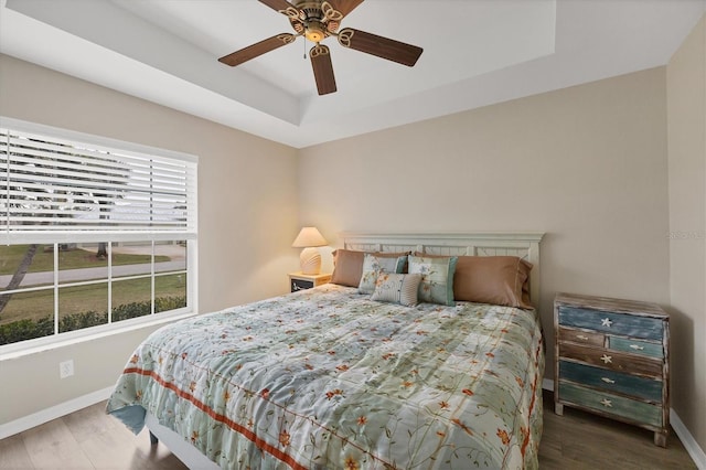 bedroom featuring a raised ceiling, ceiling fan, dark wood-type flooring, and multiple windows