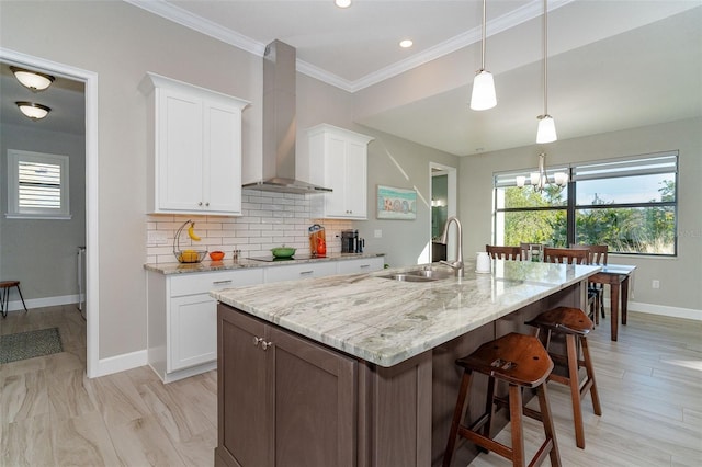 kitchen with a center island with sink, wall chimney range hood, black electric cooktop, white cabinetry, and sink