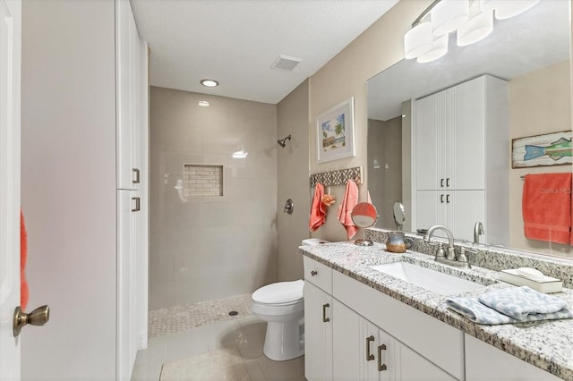 bathroom with toilet, a tile shower, tile patterned floors, a textured ceiling, and vanity