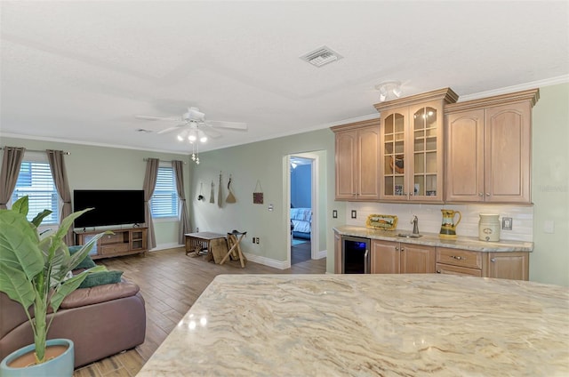 kitchen featuring tasteful backsplash, beverage cooler, light stone countertops, ornamental molding, and sink