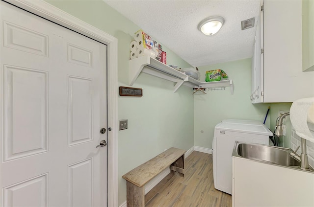 clothes washing area featuring a textured ceiling, cabinets, washing machine and clothes dryer, sink, and light wood-type flooring