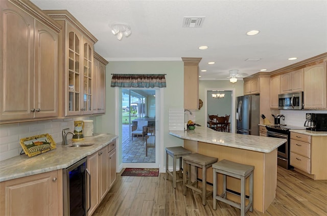 kitchen with a breakfast bar, appliances with stainless steel finishes, a sink, a peninsula, and wine cooler