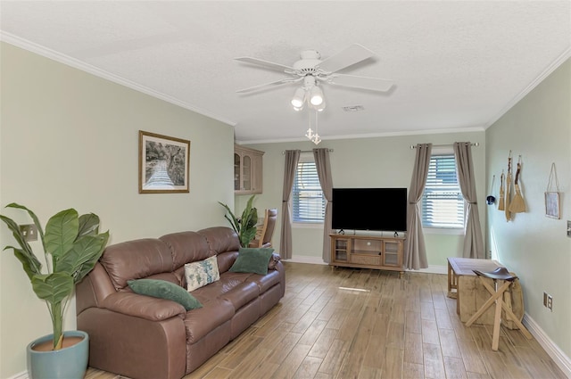 living room with a ceiling fan, visible vents, light wood-style flooring, baseboards, and ornamental molding