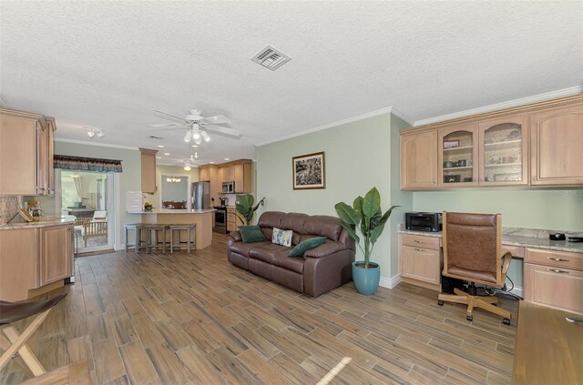office featuring crown molding, light wood-style flooring, built in desk, visible vents, and a ceiling fan