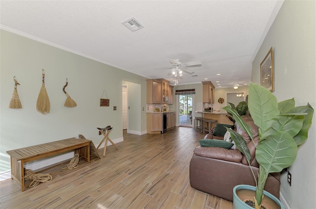 living room with crown molding, ceiling fan, visible vents, baseboards, and light wood-type flooring