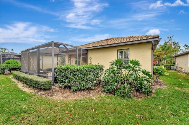 back of property with central AC, glass enclosure, and a lawn