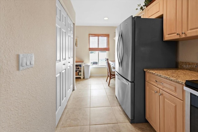 kitchen with stainless steel fridge, light stone countertops, light tile patterned flooring, and light brown cabinets