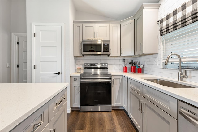 kitchen featuring lofted ceiling, sink, stainless steel appliances, light stone countertops, and decorative backsplash