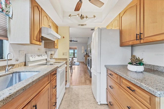 kitchen featuring sink, ceiling fan, a tray ceiling, light stone countertops, and white appliances