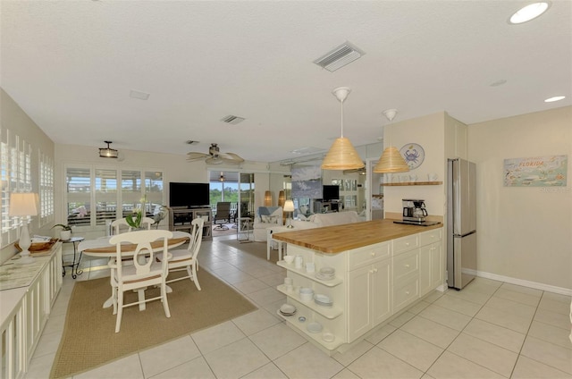 kitchen featuring a textured ceiling, wood counters, stainless steel fridge, light tile patterned flooring, and ceiling fan