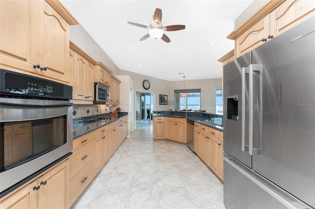 kitchen featuring stainless steel appliances, decorative backsplash, decorative light fixtures, light brown cabinetry, and dark stone counters