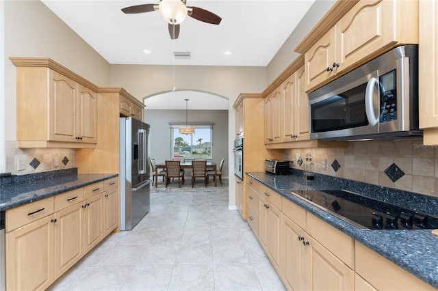 kitchen featuring decorative light fixtures, dark stone countertops, decorative backsplash, stainless steel appliances, and light brown cabinetry